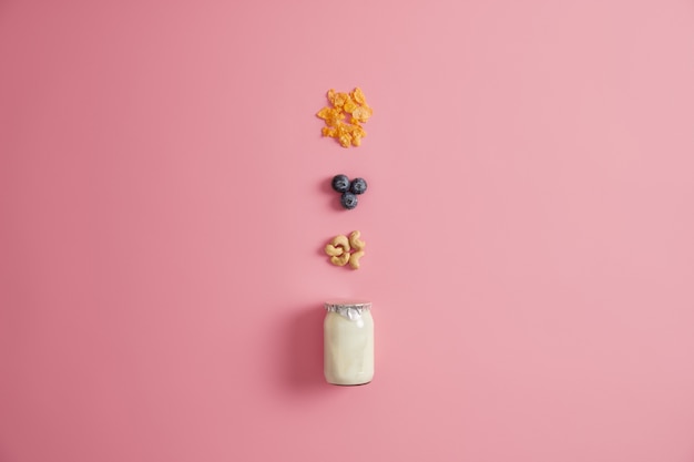 Free photo jar of fresh yoghurt, cereals, blueberry and cashew nuts for preparing delicious porridge on breakfast. ingredient for homemade sweet meal or dessert. snack and dieting concept. pink background.