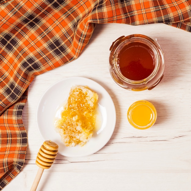 Free photo jar of honey; honeycomb; honey dipper and table cloth over white desk