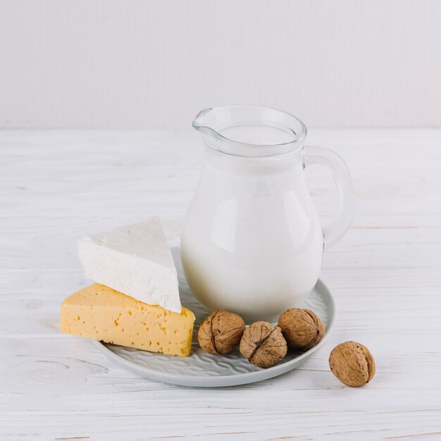 Jar of milk; cheese and walnuts on white wooden table