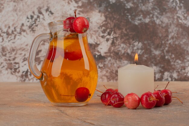 A jar of peach juice with cherries and candle on marble table.