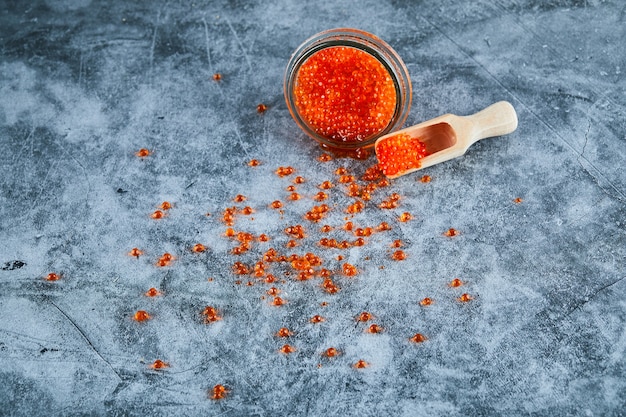 A jar of red caviar and wooden spoon on marble background.