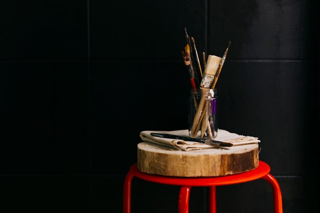 Jar with brushes near black wall