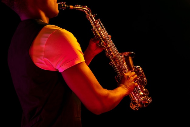 Jazz musician playing the saxophone in the studio on a neon wall