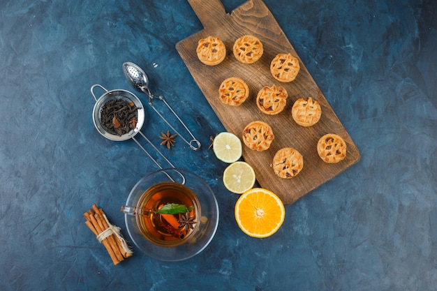 Free photo jelly filling cakes on a cutting board with a cup of tea,tea strainers,spices and citrus fruits