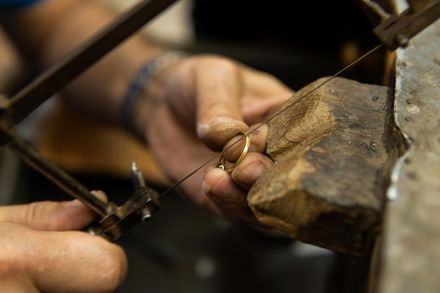 Jeweler working in his workshop cutting a gold ring with a saw