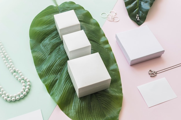 Free Photo jewelry with white boxes on green leaf over the paper backdrop