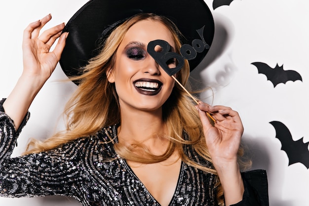 Free photo jocund blonde girl enjoying halloween party. blithesome female model in hat posing with bats on wall.