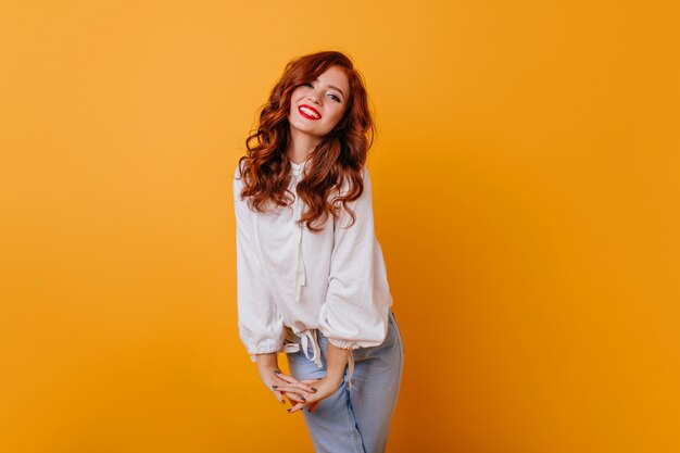 Jocund caucasin lady smiling on orange wall. Indoor photo of refined curly woman in elegant white blouse.