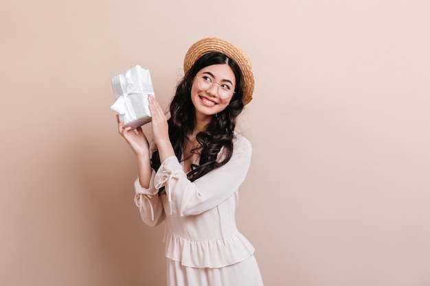 Jocund chinese woman holding birthday present. Pretty curly asian woman posing with gift.