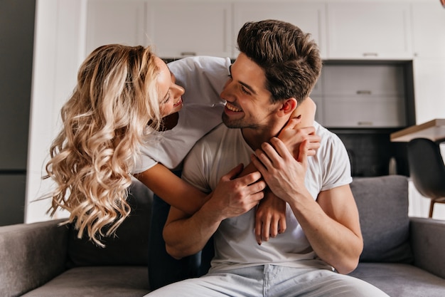 Free photo jocund curly woman embracing husband with love. brunette man looking at girlfriend with smile.