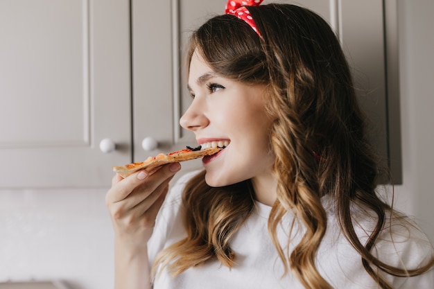 Free photo jocund dark-haired woman enjoying fast food. indoor close-up shot of elegant girl eating pizza.