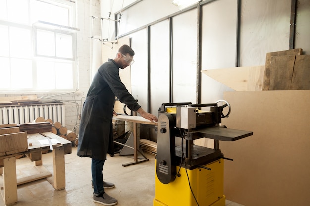 Free photo jointer in protective workwear processing wood on stationary power tool