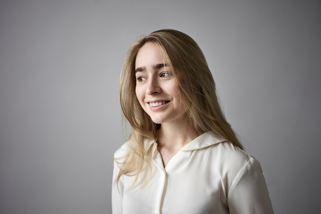 Joy, happiness and positive feelings concept. Portrait of fair haired friendly young female in stylish white shirt smiling happily, rejoicing at good news, present, exams or success at work