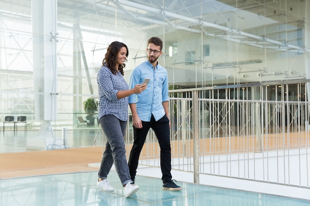 Joyful colleagues in casual looking at cellphone screen