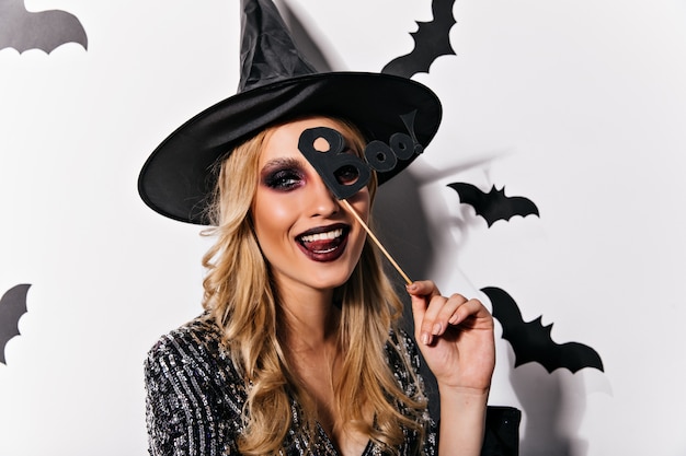 Joyful european woman playfully posing in halloween. Adorable young witch with black makeup expressing happiness.