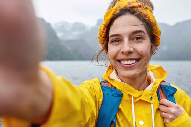 Free Photo joyful female has expedition tour, makes selfie portrait, stretches hand in camera, smiles broadly