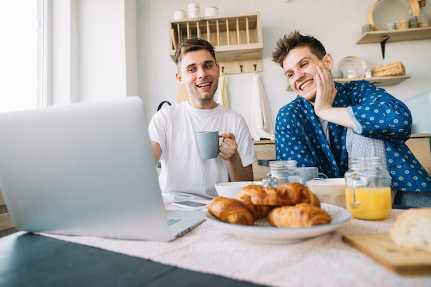 Free photo joyful friends enjoying breakfast while watching something on laptop