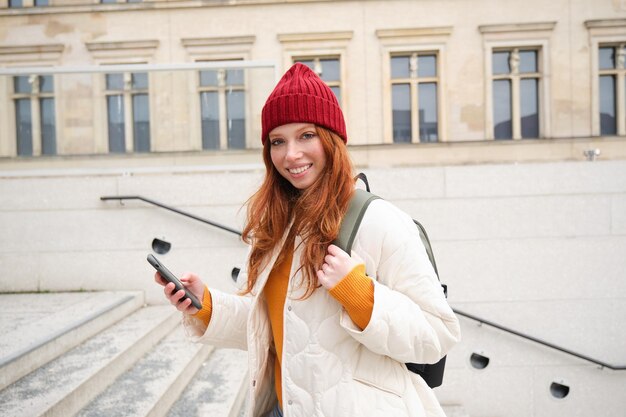 Free Photo joyful girl tourist looks at mobile phone texts message on smartphone social media application walks