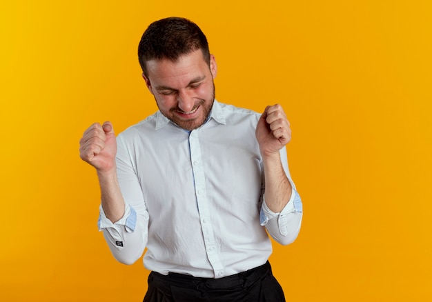 Joyful handsome man keeps fists with closed eyes isolated on orange wall