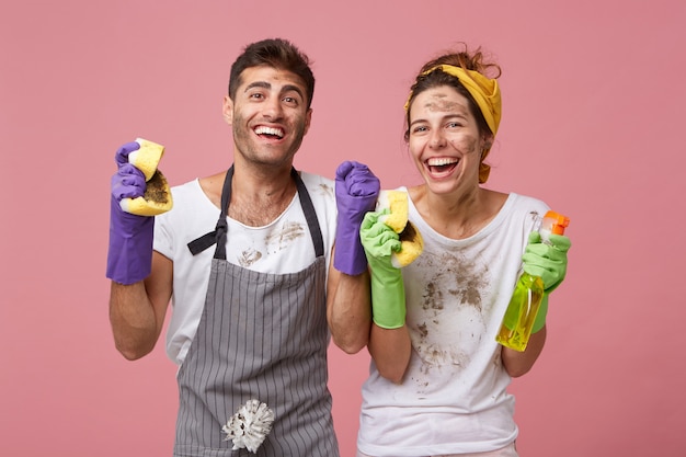 Joyful happy family couple clenching their fists with excitement being glad to clean all rooms of their house rejoicing their results. Successful male and female workers from cleaning service