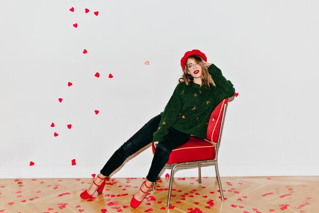 Free photo joyful lady in black pants sitting on chair with pensive face expression