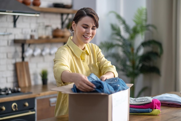 Joyful lady packing sorted clothes into a carton