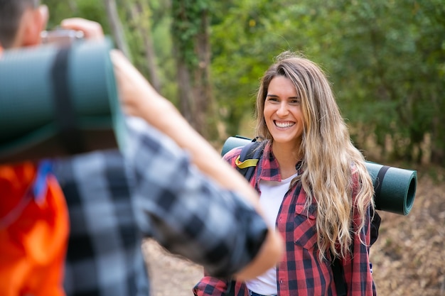 Free photo joyful long-haired woman posing and laughing when her cropped boyfriend taking photo with camera. happy hikers traveling together on nature. backpacking tourism, adventure and summer vacation concept