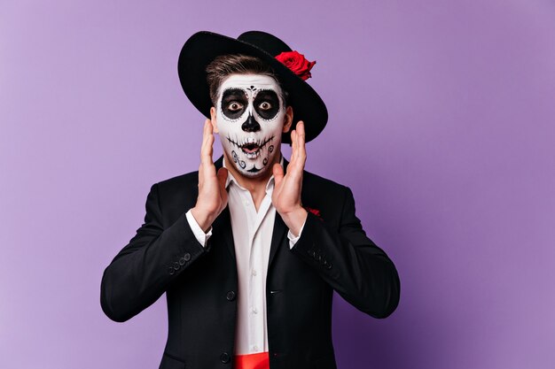 Joyful man with Halloween makeup in shock looks into camera, posing on purple background.