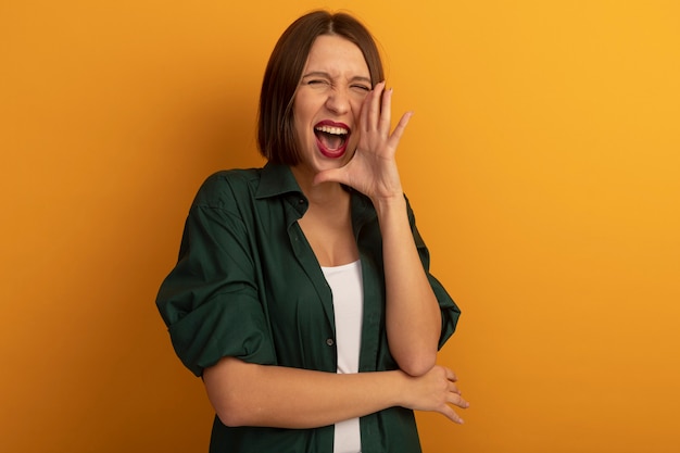 Free Photo joyful pretty woman holds hand close to mouth calling someone isolated on orange wall