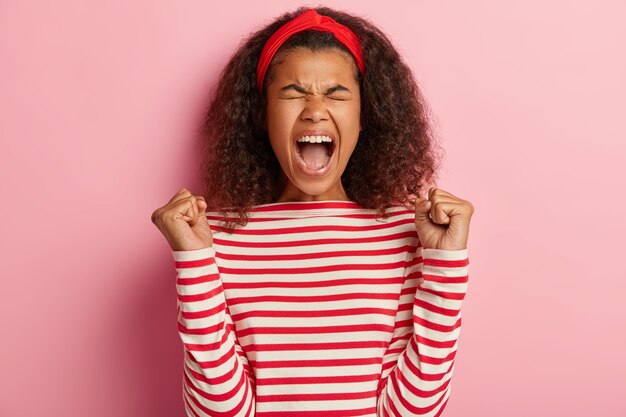 Joyful teenage girl with curly hair posing in striped red sweater