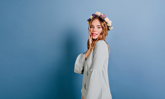 Free photo joyful white woman with beautiful flowers in hair posing on blue wall