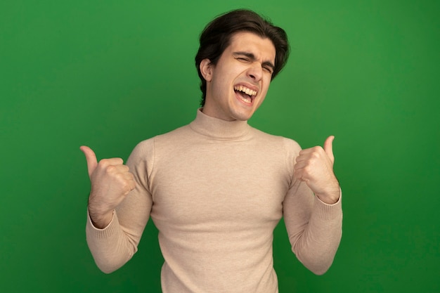 Free Photo joyful with closed eyes young handsome guy showing thumbs up isolated on green wall