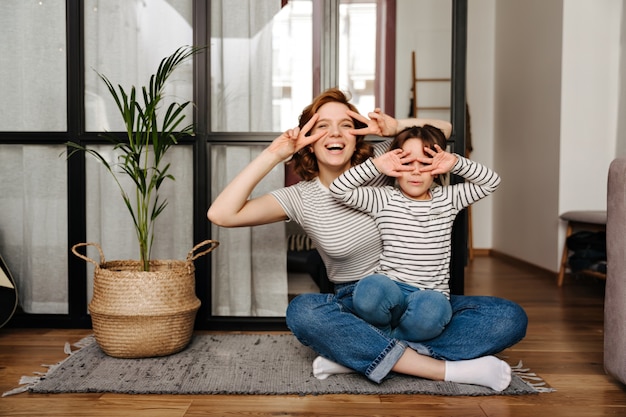 Free photo joyful woman and her daughter having fun in living room and showing signs of peace.