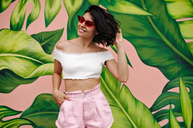 Free photo joyful woman in pink shorts standing near colorful graffiti