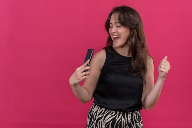 Joyful woman wearing black undershirt liten music from phone on pink wall