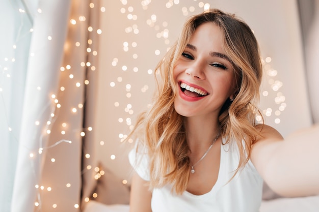 Free photo joyful woman with sincere smile posing in her room. blonde caucasian girl expressing happiness