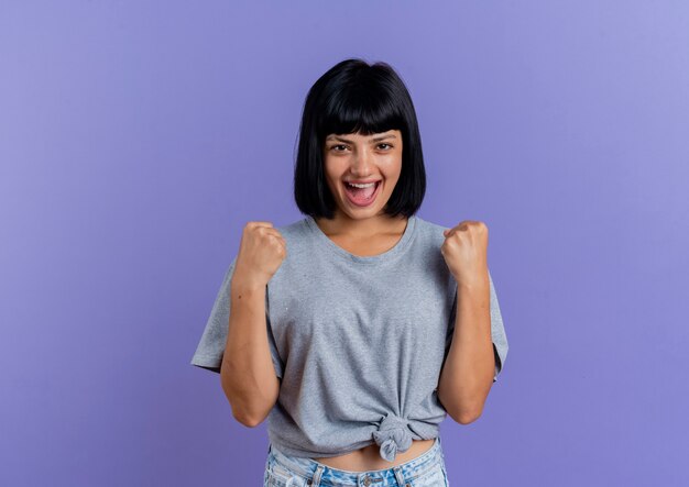 Joyful young brunette caucasian girl keeps fists looking  