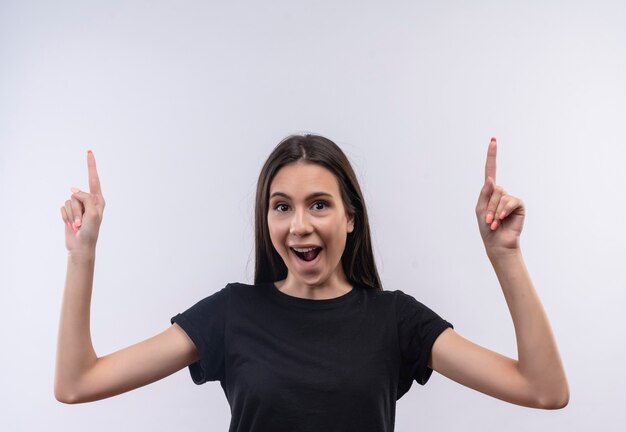 joyful young caucasian girl wearing black t-shirt points to up on isolated white wall