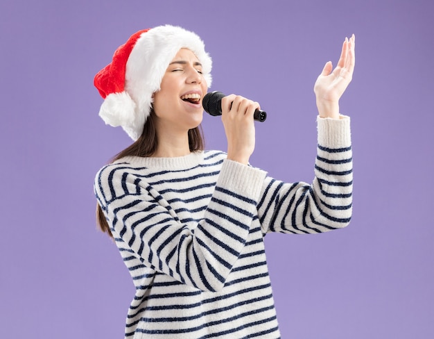 Free photo joyful young caucasian girl with santa hat holding mic pretending to sing