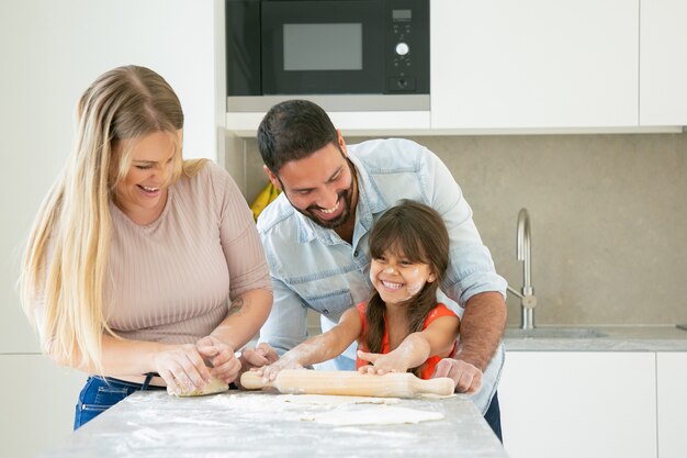 Joyful young couple and girl with flower powder on face laughing while baking together.