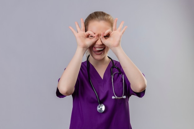 Free Photo joyful young doctor wearing purple medical gown and stethoscope shows look gesture on isolated white wall