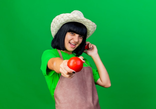 Free Photo joyful young female gardener in uniform wearing gardening hat holds tomatoes