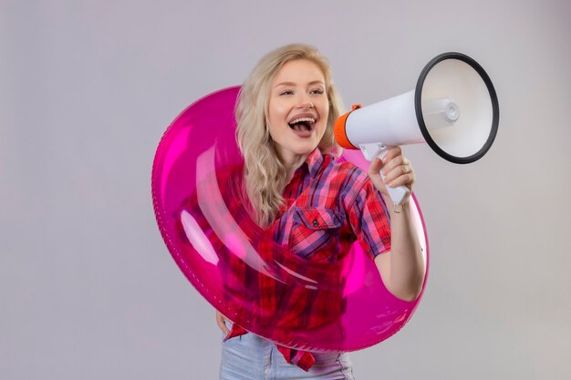 Joyful young female traveler wearing red shirt in inflatable ring speakes through loudspeakers on isolated white wall