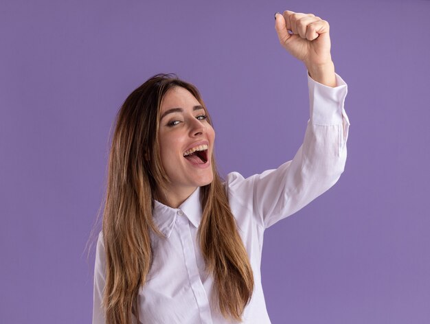 Joyful young pretty caucasian girl stands with raised fist up on purple 