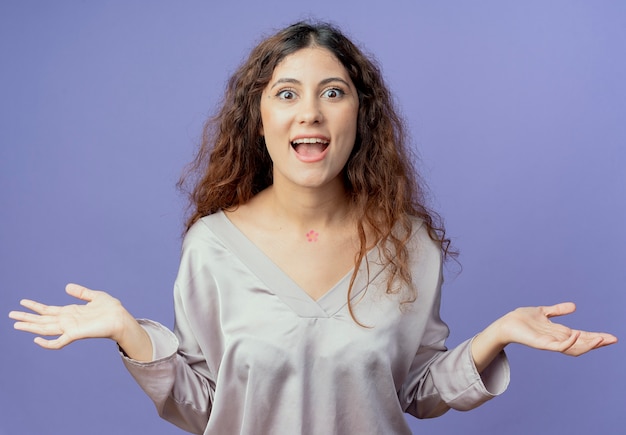 Joyful young pretty girl spreads hands isolated on blue background