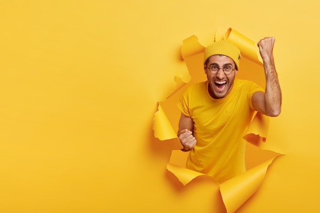 Joyous cheering man posing through torn paper