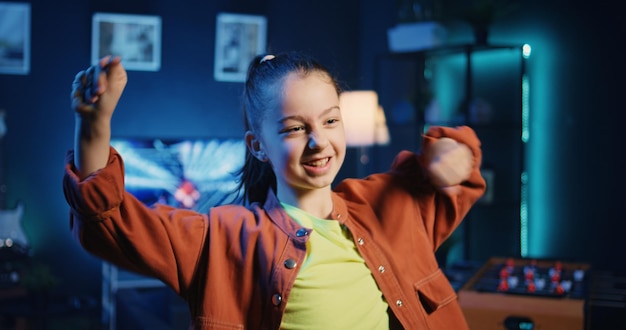 Free photo joyous kid mesmerizing her followers with incredible dance moves in neon lit home studio