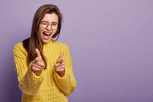 Joyous lovely female blinks eyes, exclaims from happiness, points at you, demonstrates her choice