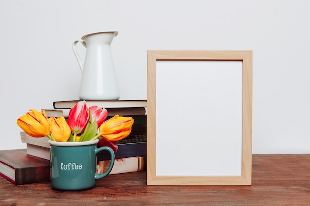 Jug on books near flowers and frame