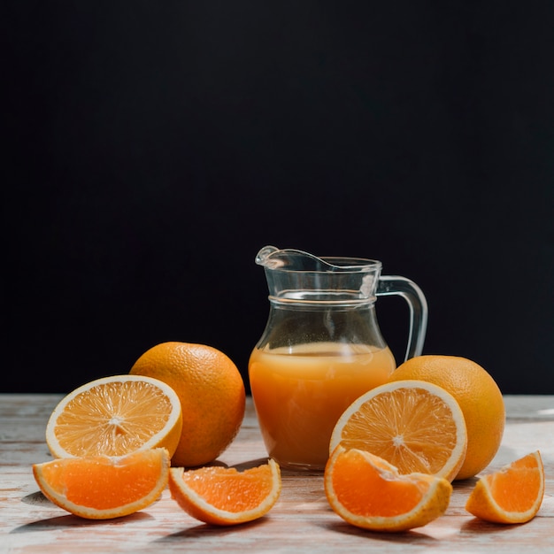 Jug of delicious orange juice surrounded by glasses and oranges front view